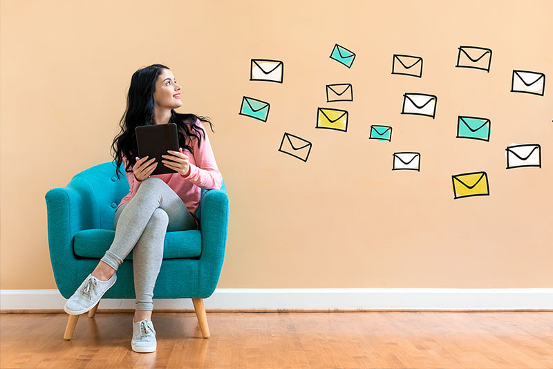 a woman sitting in a chair with a laptop and email symbols flying out from behind her.