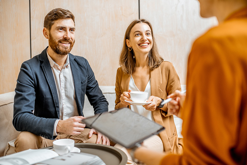 An excited couple having tea and talking to an advisor.